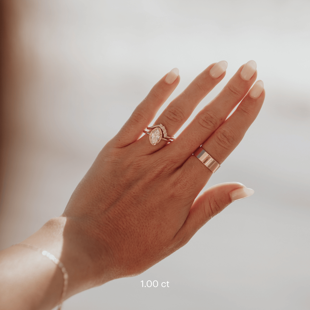 The Maren Ring in 14k yellow gold featuring a lab-grown marquise diamond center stone set with six prongs in a high polish gold halo, worn on the ring finger alongside a diamond accent band, with a wide gold band worn on another finger.
