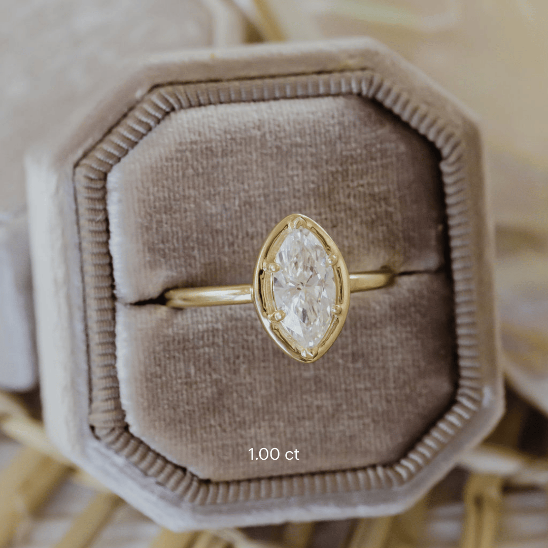 The Maren Ring in 14k yellow gold featuring a lab-grown marquise diamond center stone set with six prongs in a high polish gold halo, displayed in a taupe velvet ring box. The Maren Marquise Ring features a 14k gold ring with a marquise center stone set with six prongs with a high polish gold halo. The entire design is set flush to the finger. This ring is made-to-order based on the selected customizations.