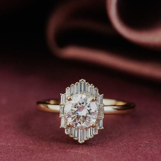 The North Star Ring in 14k yellow gold, featuring a round cut center stone with a baguette diamond halo, shown from a front-facing angle on a deep red surface.