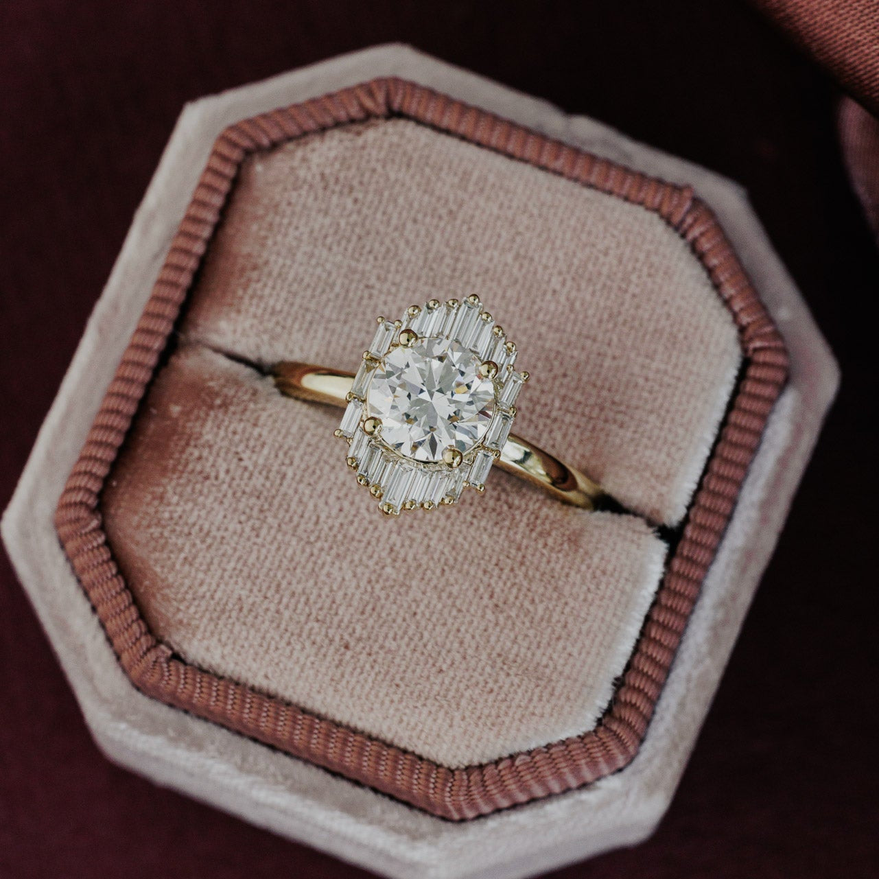 The North Star Ring in 14k yellow gold, featuring a round cut center stone with a baguette diamond halo, displayed in an octagonal velvet ring box.
