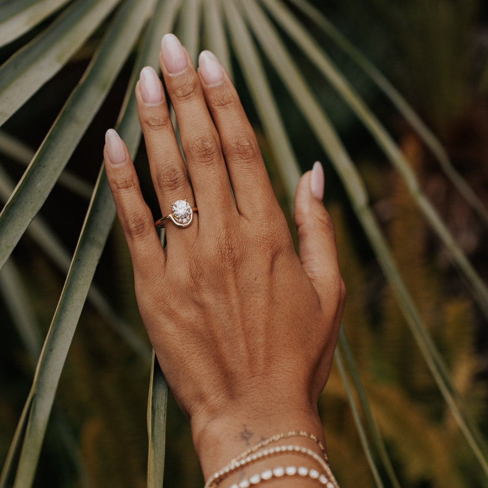 The Palma Round Ring in 14k yellow gold featuring a lab-grown round diamond center stone with round diamond arc accent, worn on the ring finger alongside stacked gold bracelets.