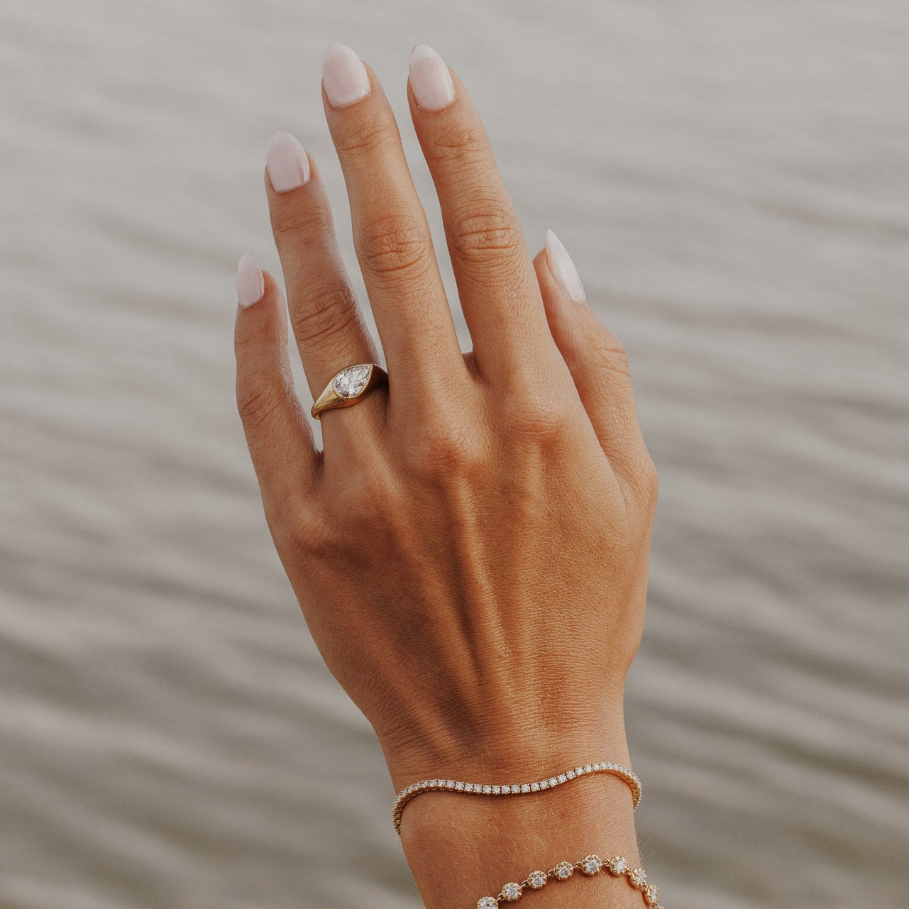 The Santorini Pear Ring in 14k yellow gold featuring a lab-grown pear diamond bezel set on a tapered band, worn on the ring finger alongside a diamond tennis bracelet.