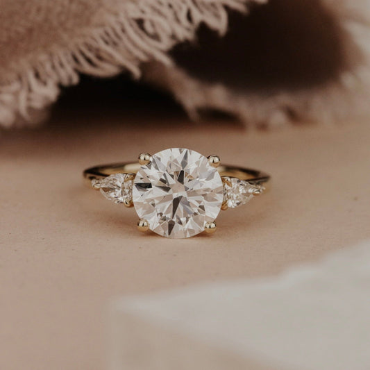 The Toula Round Ring in 14k yellow gold featuring a lab grown diamond round center stone set in four prongs, flanked by pear and round natural diamond side stones on a high polish band.