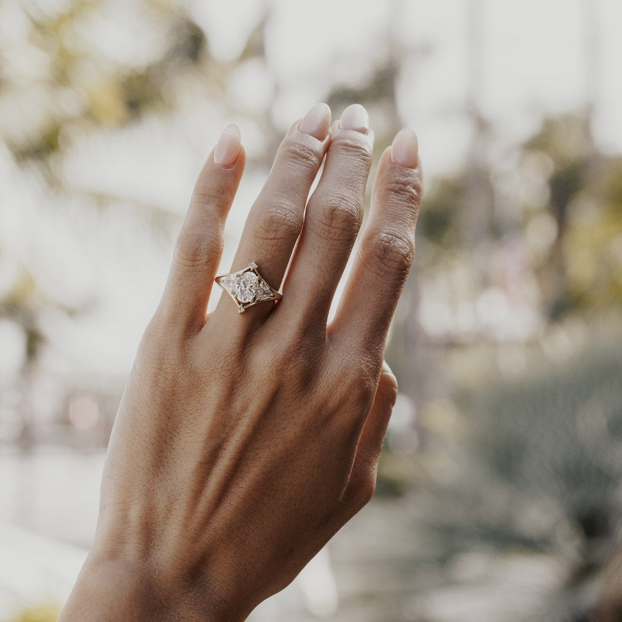 The Tulum Oval Ring in 14k yellow gold featuring a lab-grown oval diamond center stone with trillion and princess cut diamond accents in a geometric halo, worn on the ring finger.