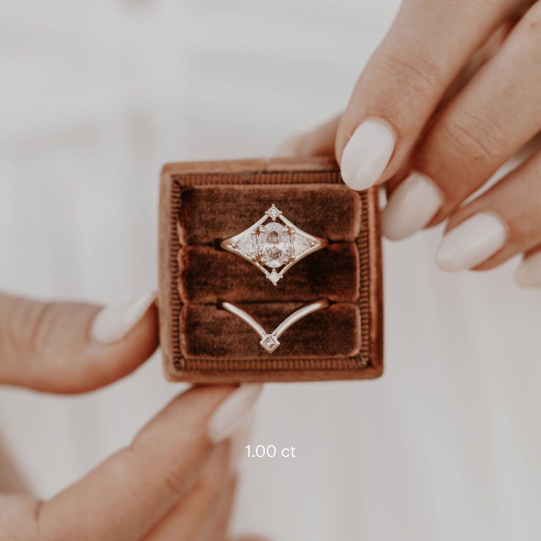 The Tulum Oval Ring in 14k yellow gold featuring a lab-grown oval diamond center stone with trillion and princess cut diamond accents in a geometric halo, displayed in a brown velvet ring box alongside a contoured matching band.