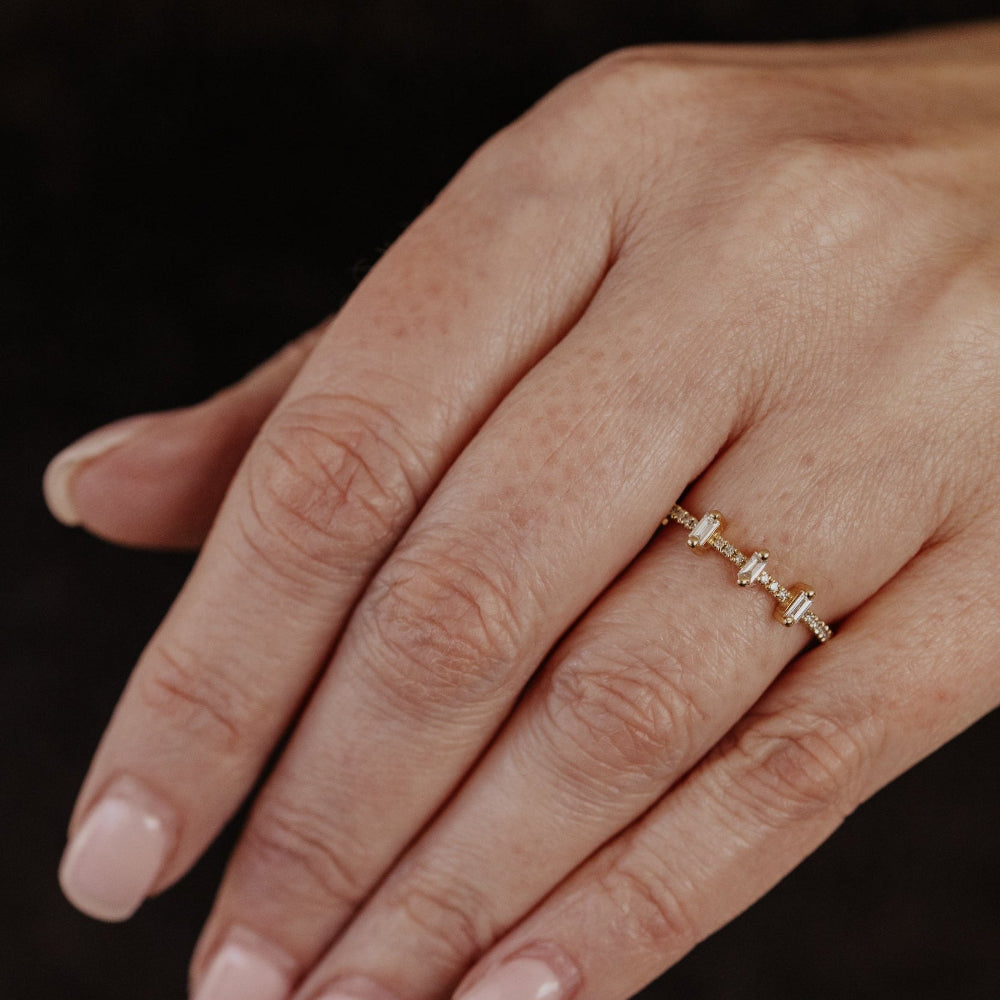 Hand wearing a gold wedding band with baguette diamonds on a dark background.