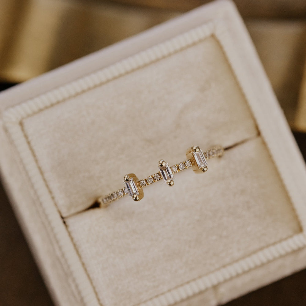 Gold ring with baguette diamonds in a beige jewelry box.