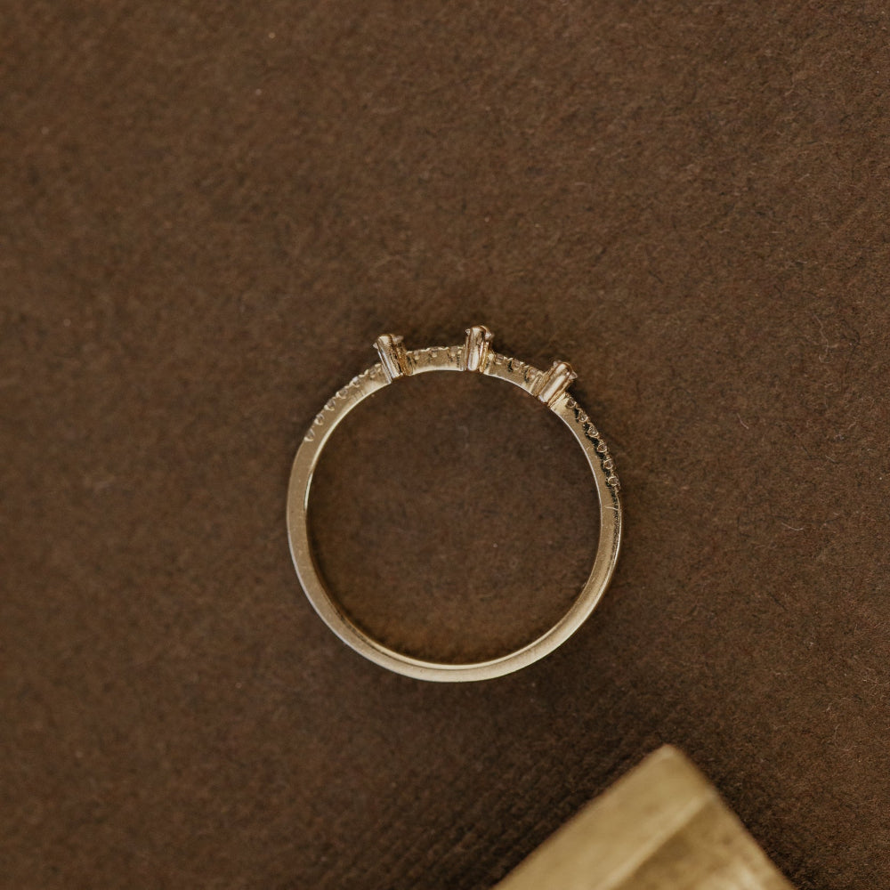 Gold wedding band with small stones on a brown textured surface.