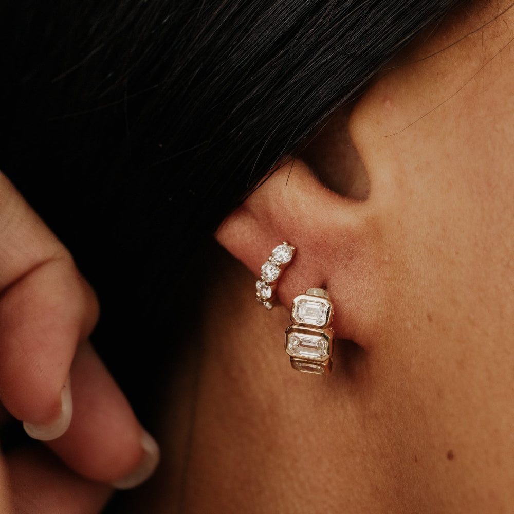 Close-up of an ear wearing a yellow gold earring with three emerald cut lab grown diamonds.