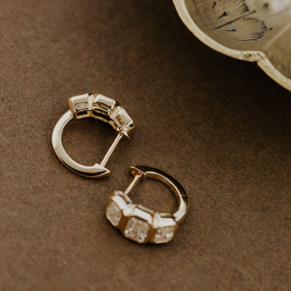 Gold hoop earrings with three lab grown diamonds on a brown surface.