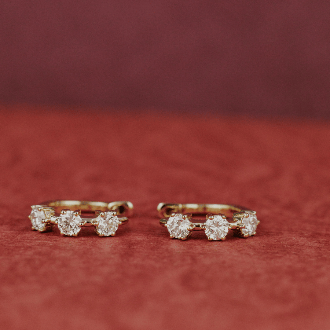 14k gold three prong set lab grown hoop earrings showcased on a textured red surface. 