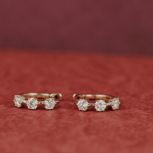 14k gold three prong set lab grown hoop earrings showcased on a textured red surface. 