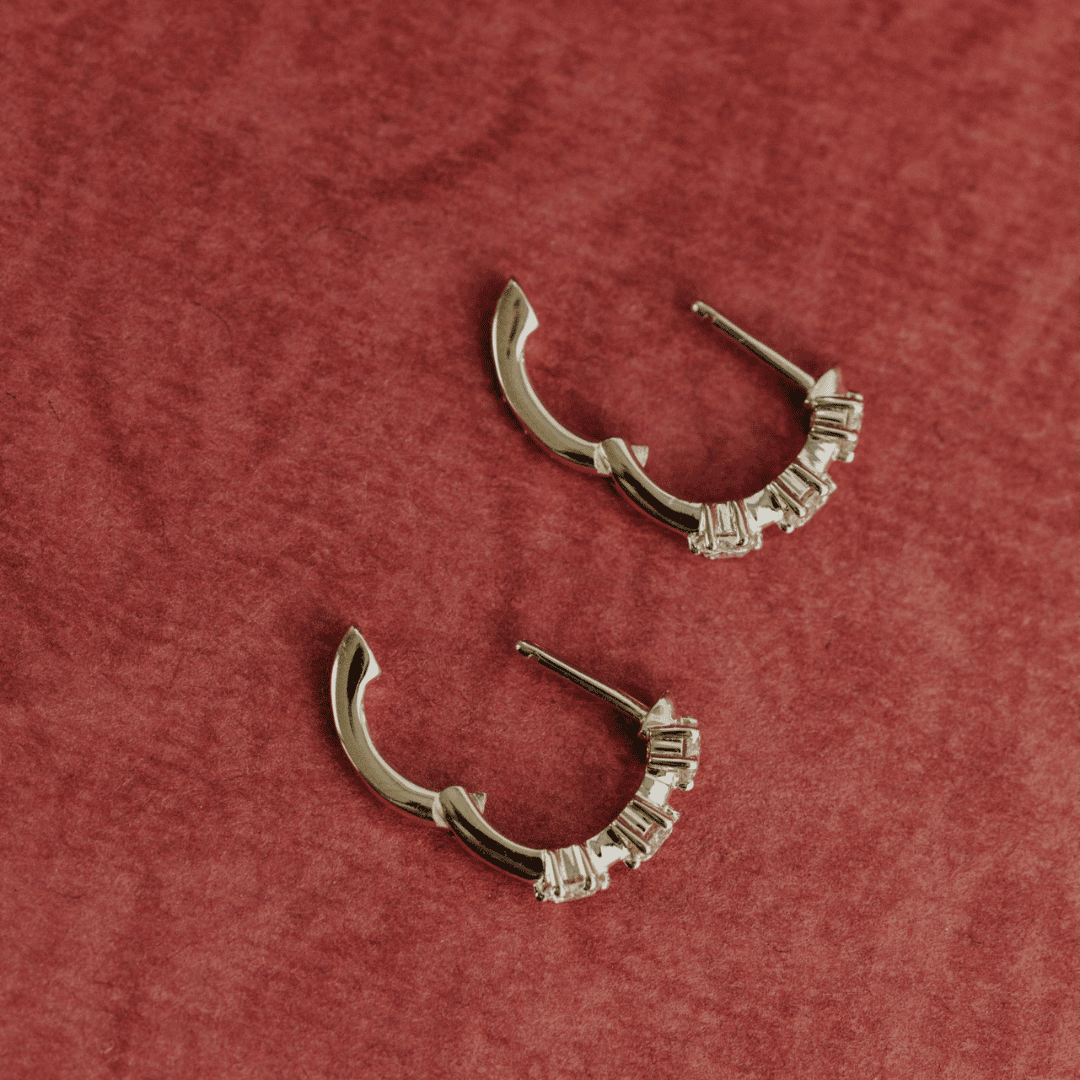 14k gold three prong set lab grown hoop earrings showcased on a textured red surface with the clasp open. 