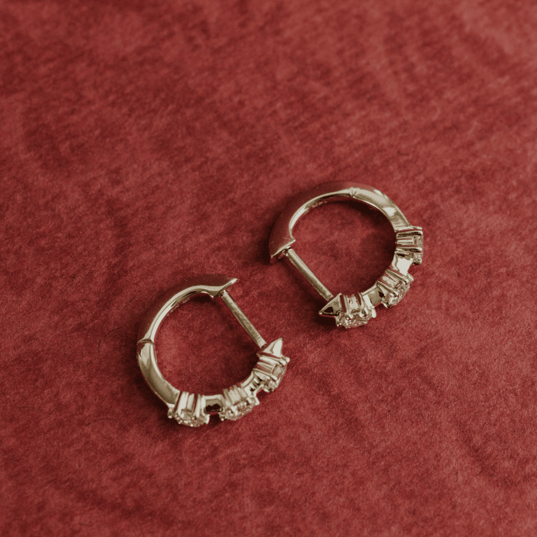 14k gold three prong set lab grown hoop earrings showcased on a textured red surface. 
