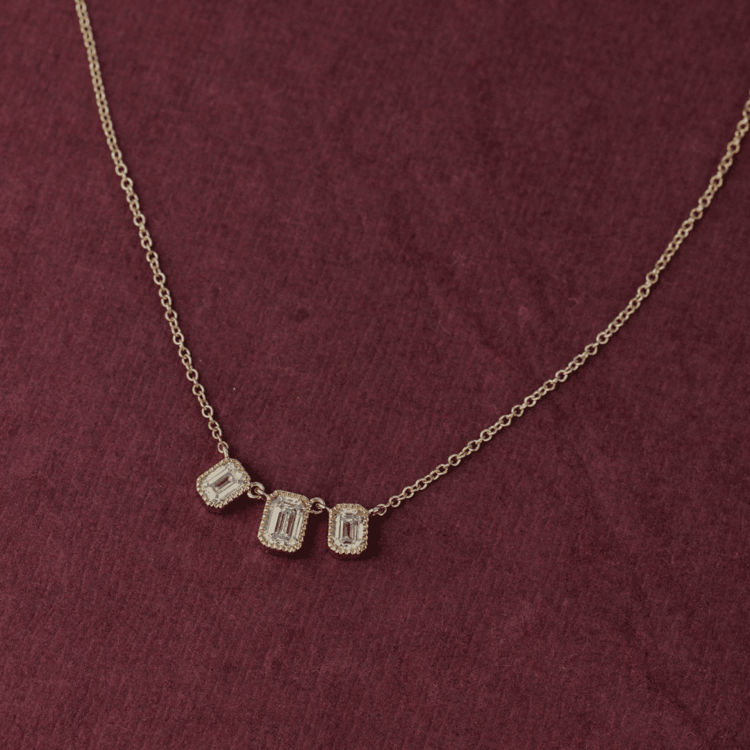 14k gold emerald cut, 3 milgrain, lab grown diamond chain bracelet showcased on a textured red surface.