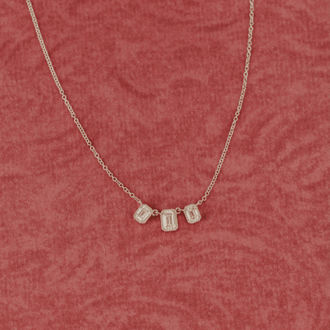 14k gold emerald cut, 3 milgrain, lab grown diamond chain bracelet showcased on a textured red surface. 