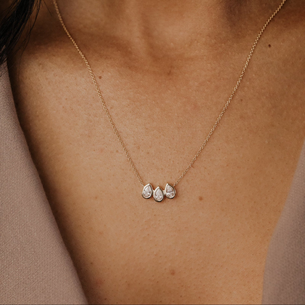 Gold necklace with three pear-shaped lab grown diamonds on a person's neck.