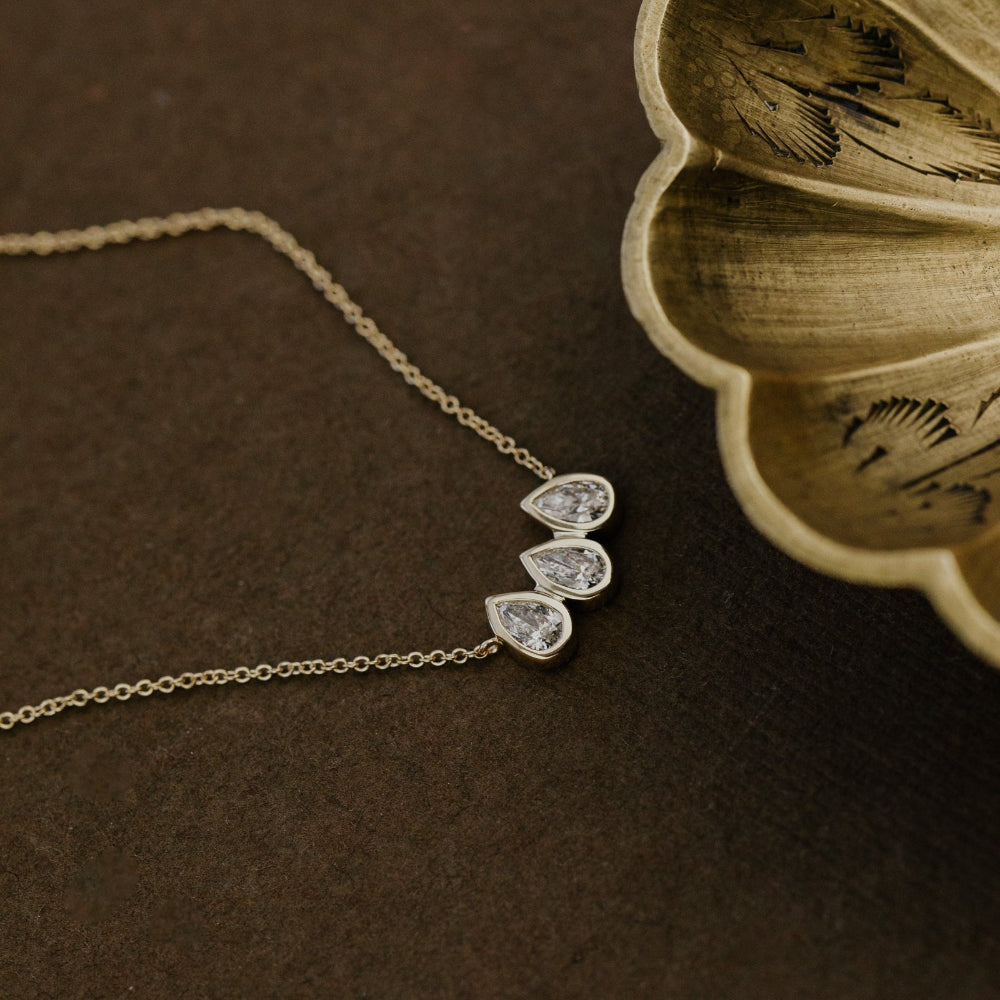 Gold necklace with three pear-shaped lab grown diamond pendants on a dark surface.