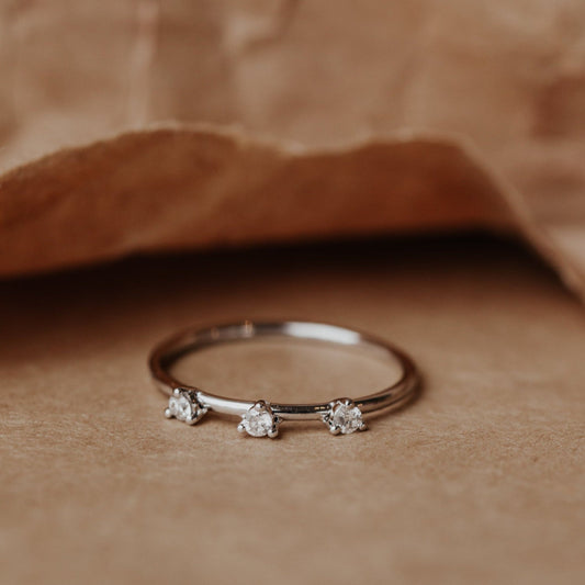 White gold wedding band with three small diamonds on a brown fabric background.