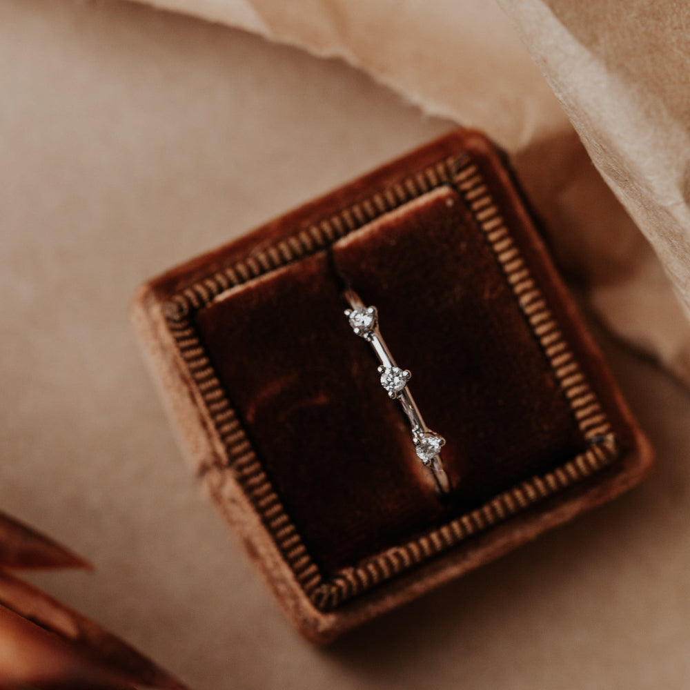 Diamond wedding band in a brown velvet box on a soft beige background.