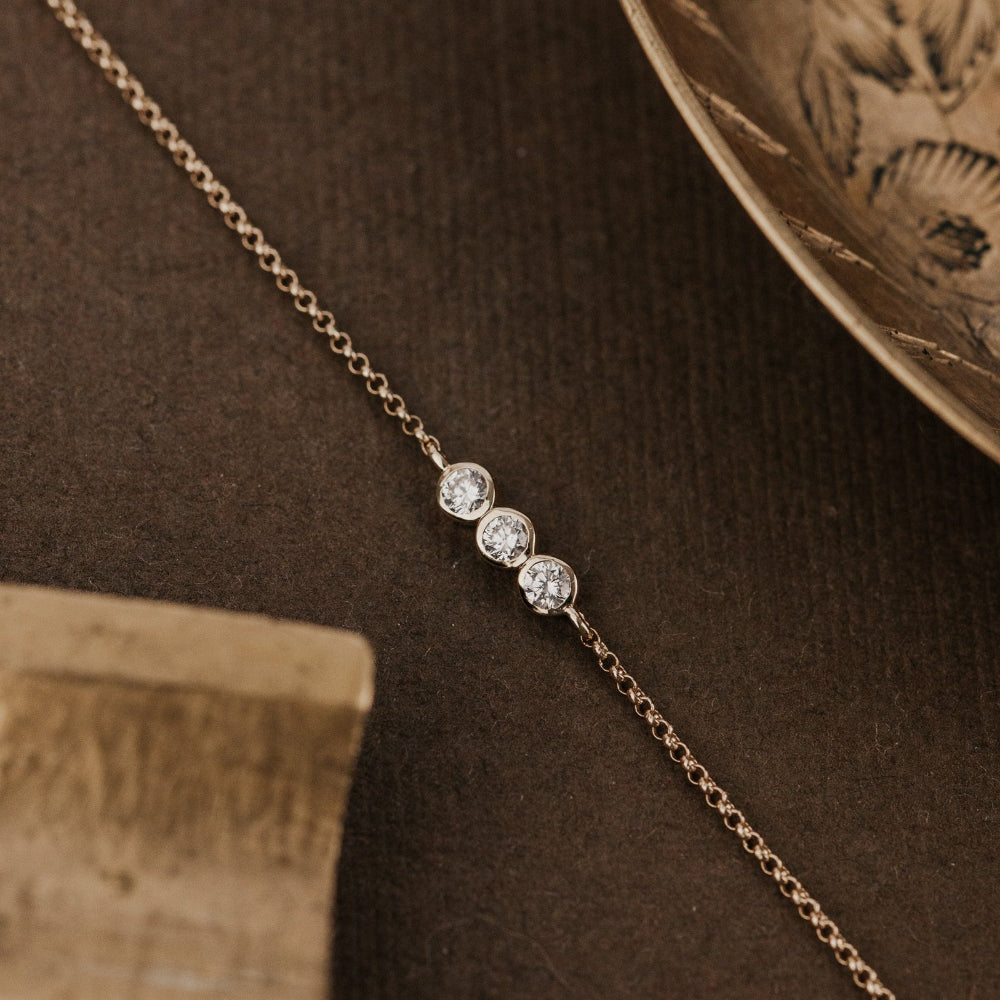 Gold bracelet with three diamonds on a brown textured surface.