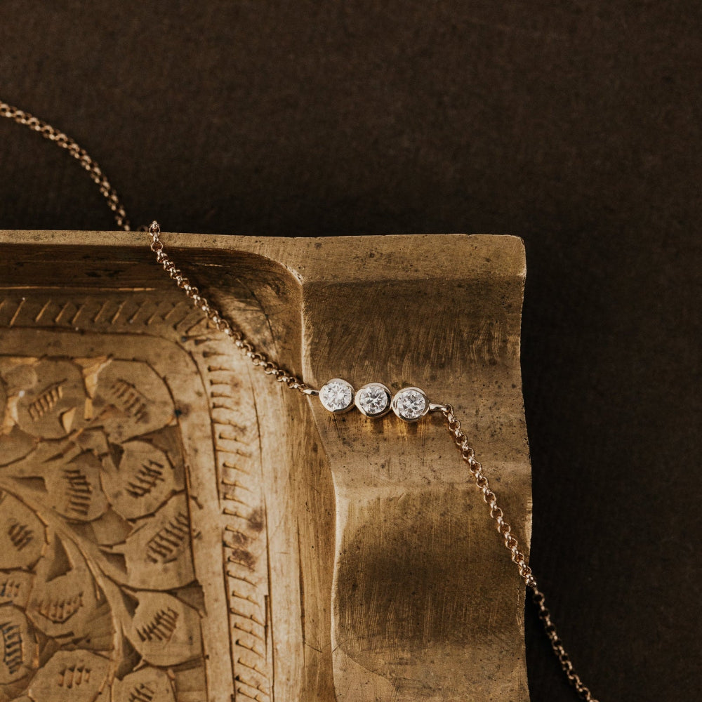 Gold bracelet with three round diamonds on a textured wooden block against a dark background.