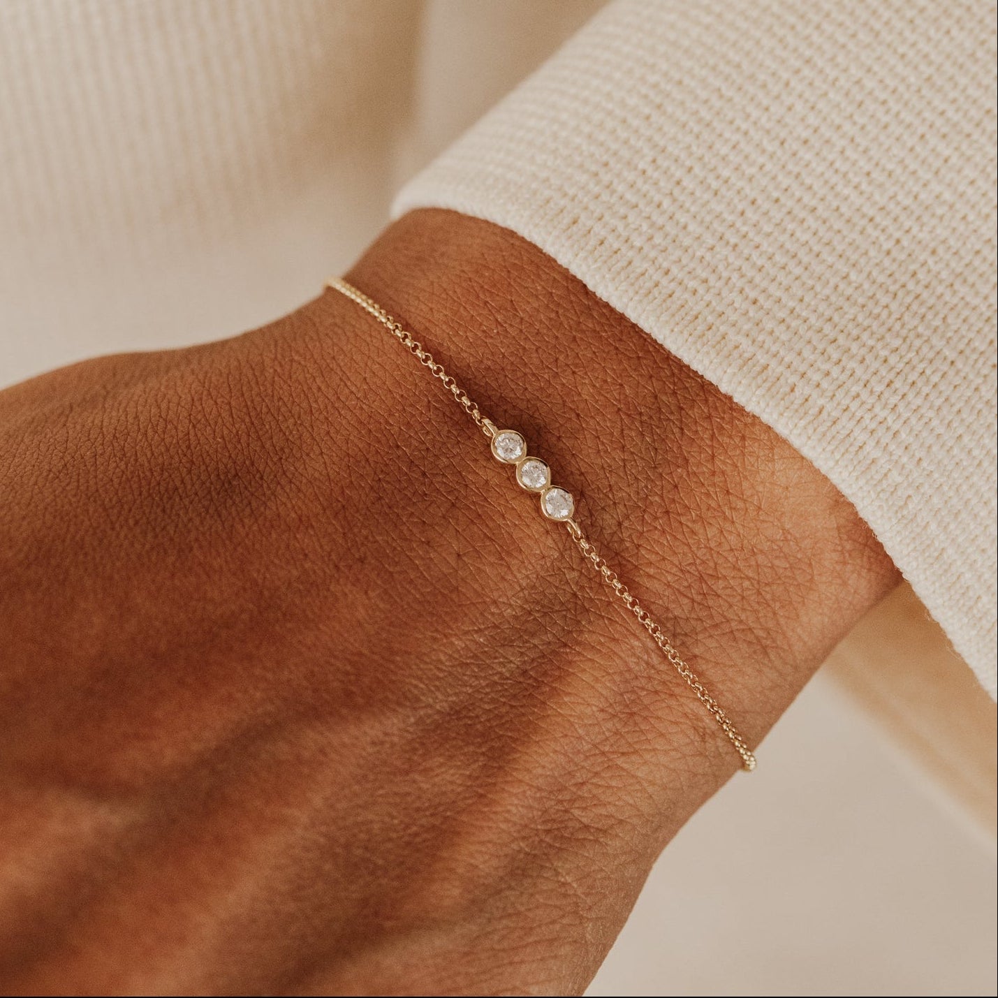 Gold bracelet on a wrist with a neutral background.