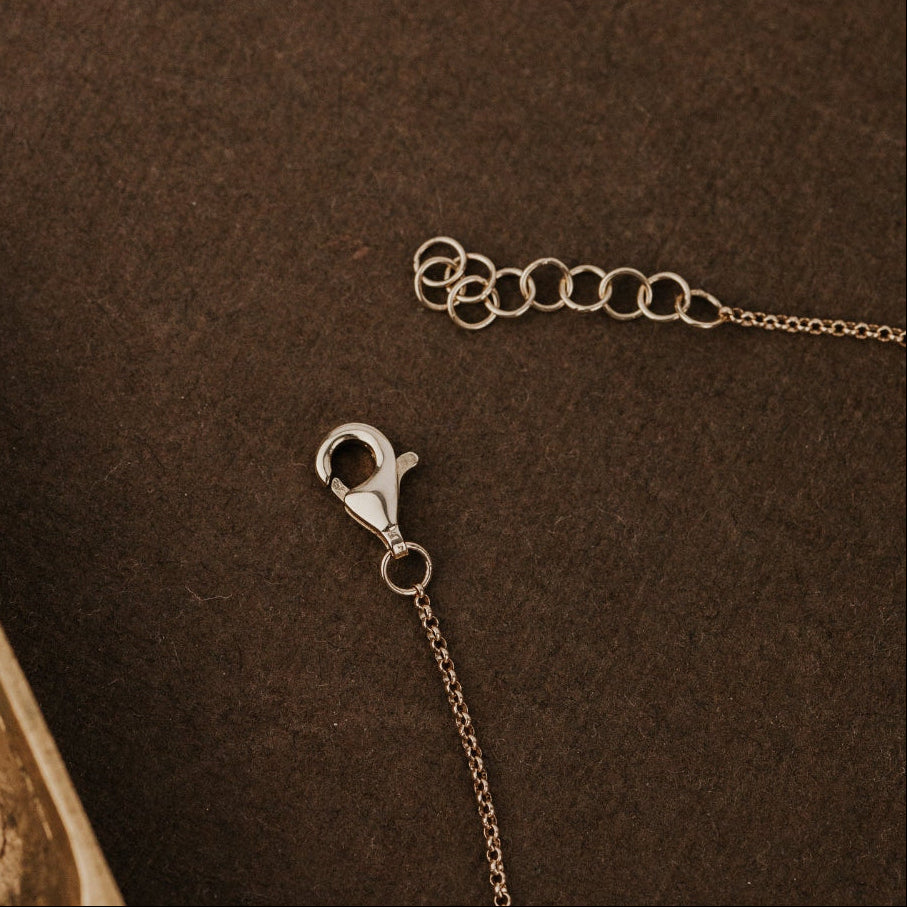 Gold bracelet with clasp on a brown textured background.