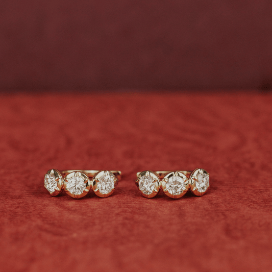 14k gold three round lab grown diamond huggie earrings showcased on a textured red surface. 