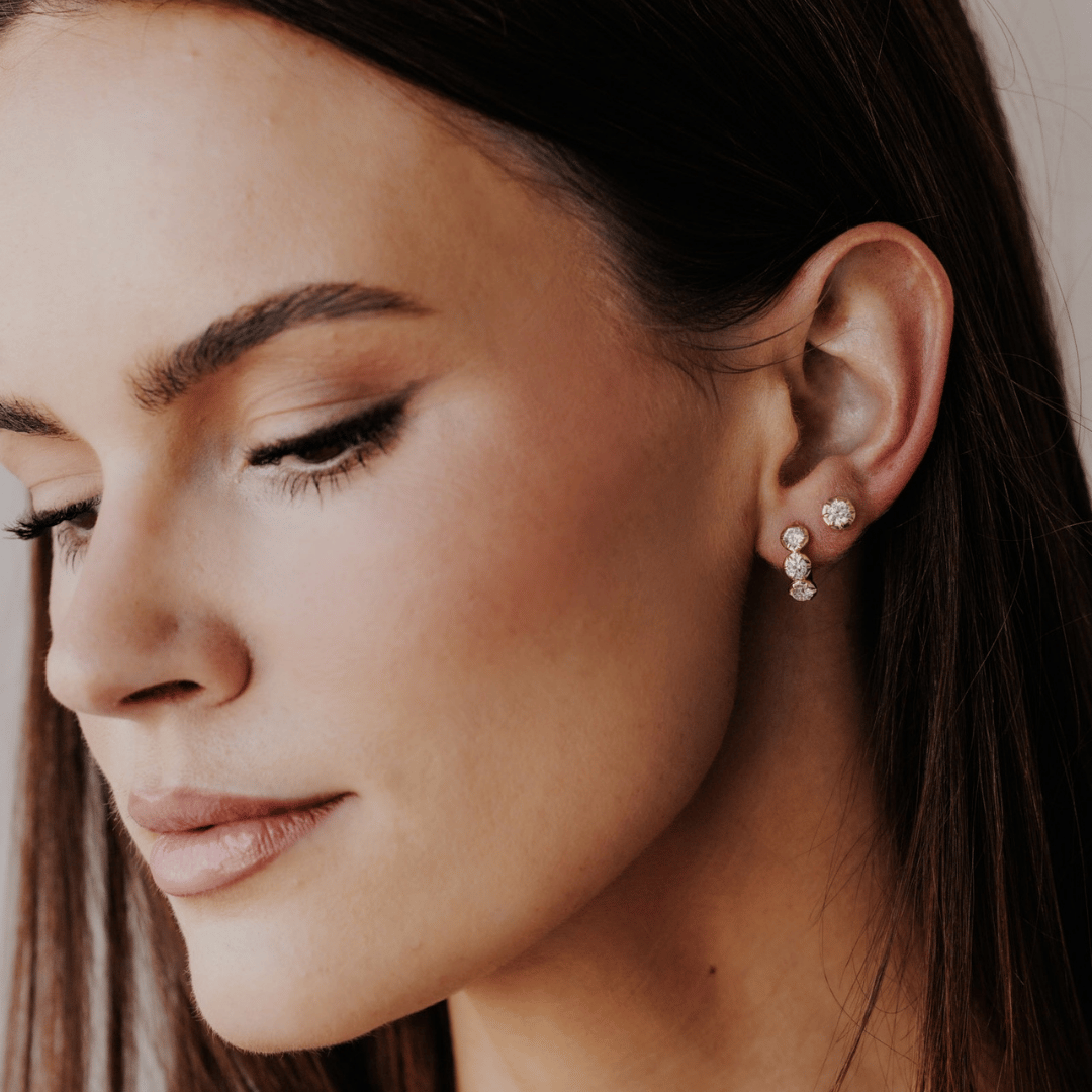 14k gold three round lab grown diamond huggie earrings showcased on a the ear of a model. 