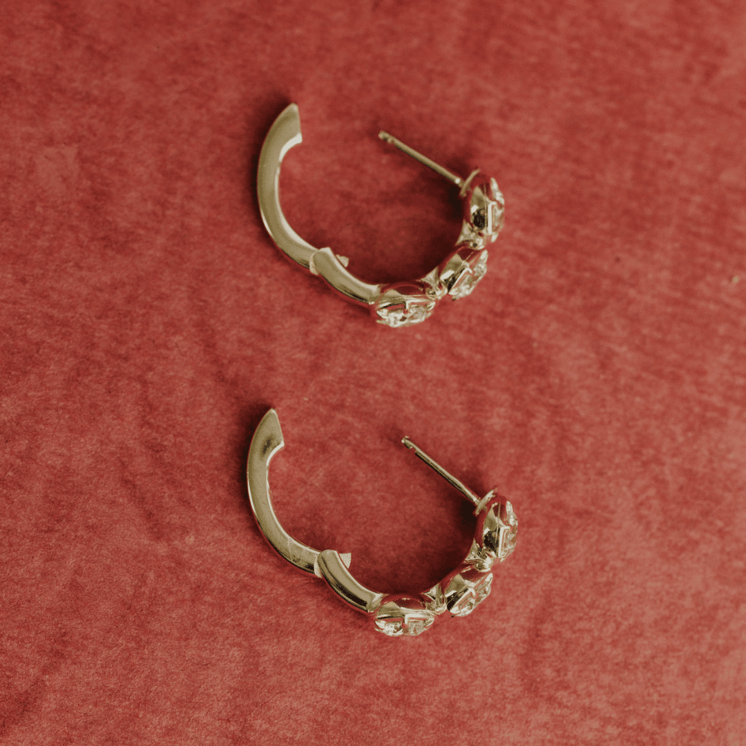 14k gold three round lab grown diamond huggie earrings showcased on a textured red surface with the clasp open. 