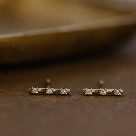 Pair of gold earrings with small diamonds on a brown surface.