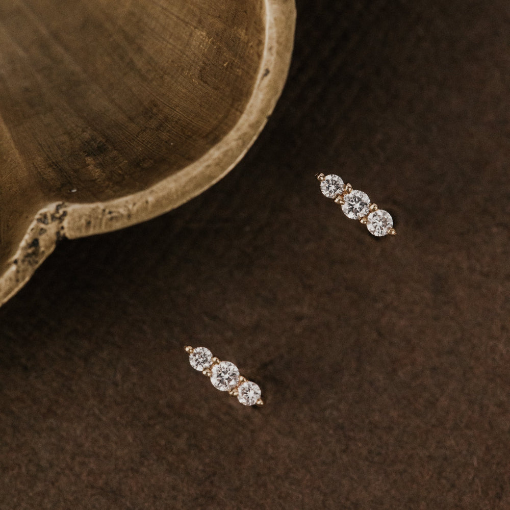 Pair of diamond earrings on a dark brown surface with a textured background.