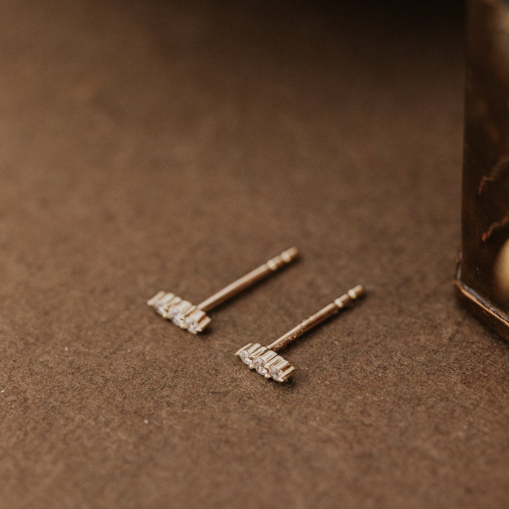 Pair of gold earrings with diamonds on a brown surface.