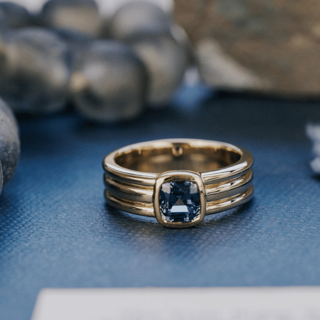 A 14k gold ring featuring a solitare Montana blue sapphire gemstone, displayed on a textured blue surface with a soft background.