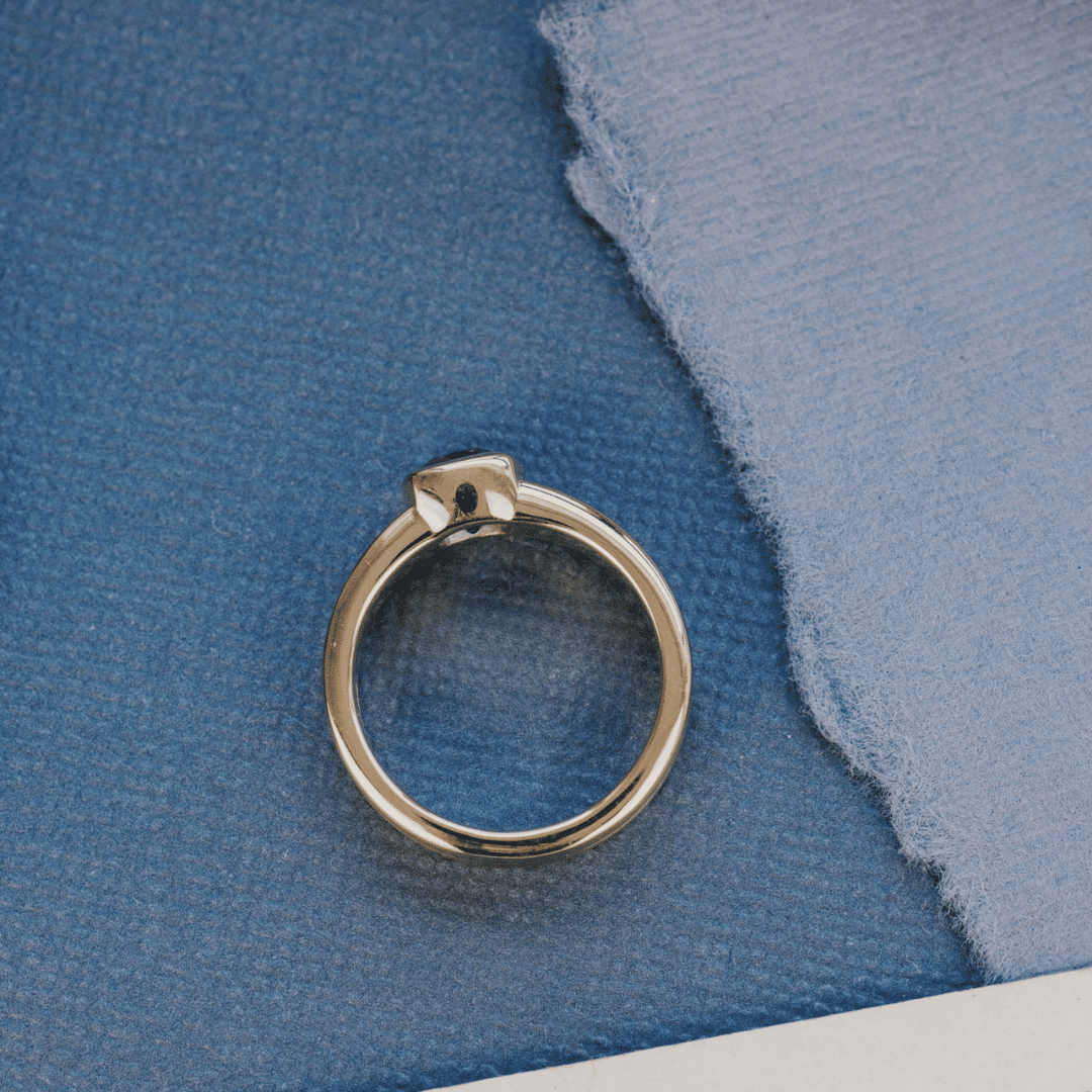 A 14k gold ring featuring a solitare Montana blue sapphire gemstone, displayed from a top-view with a textured blue surface on a beaded necklace.