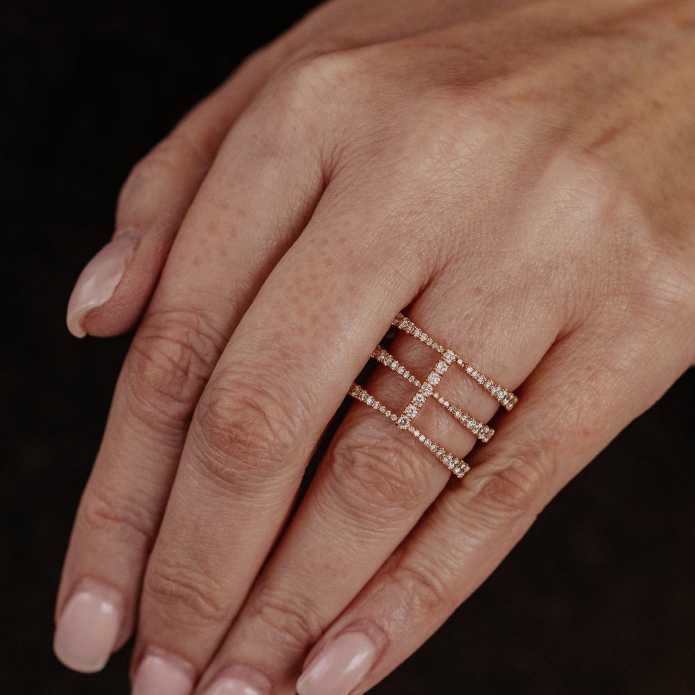Close-up of a hand wearing a delicate rose gold diamond wedding band on a dark background.