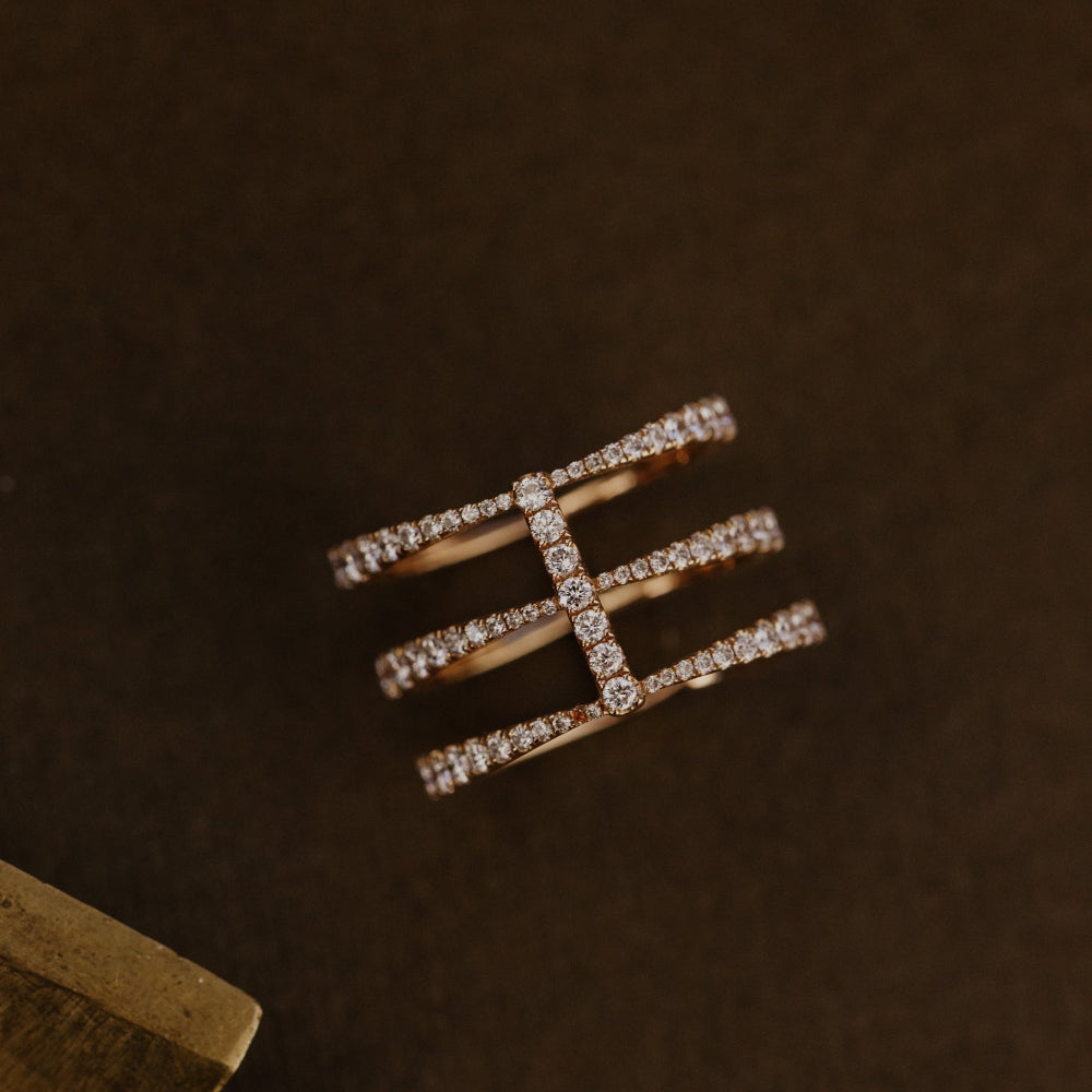Rose gold wedding band with diamonds on a dark brown background.