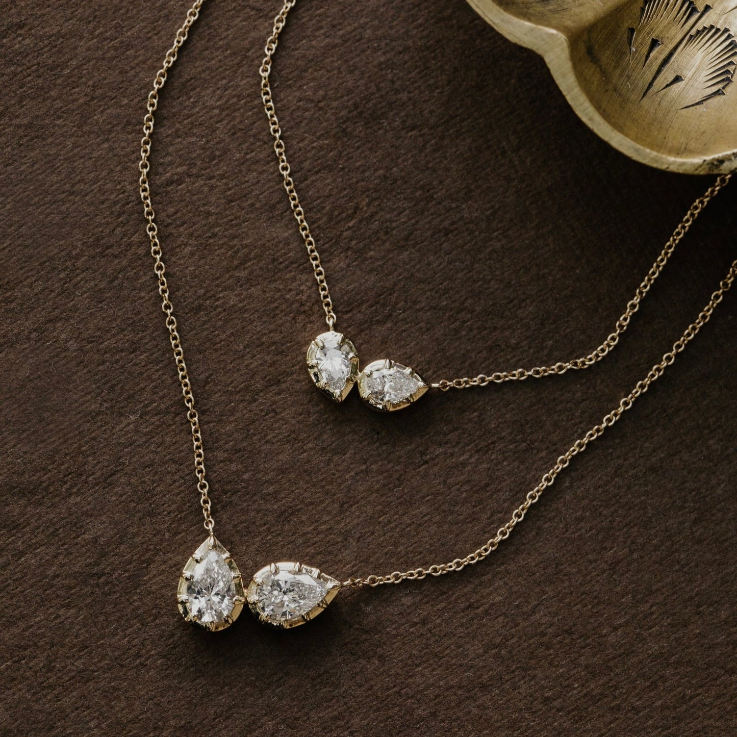 Gold necklace with two pear-shaped lab grown diamond pendants on a brown surface.