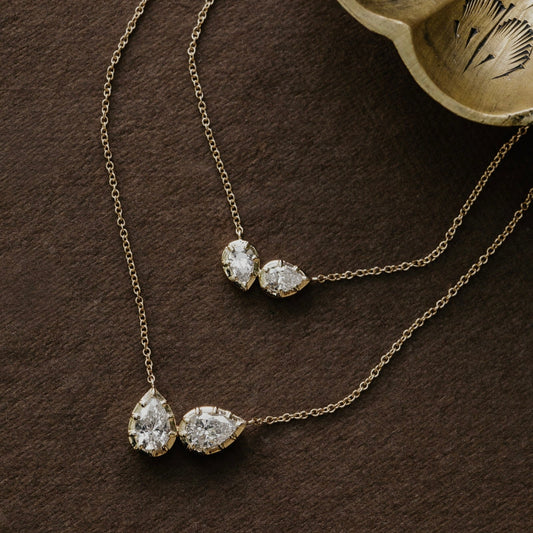 Gold necklace with two pear-shaped lab grown diamond pendants on a brown surface.
