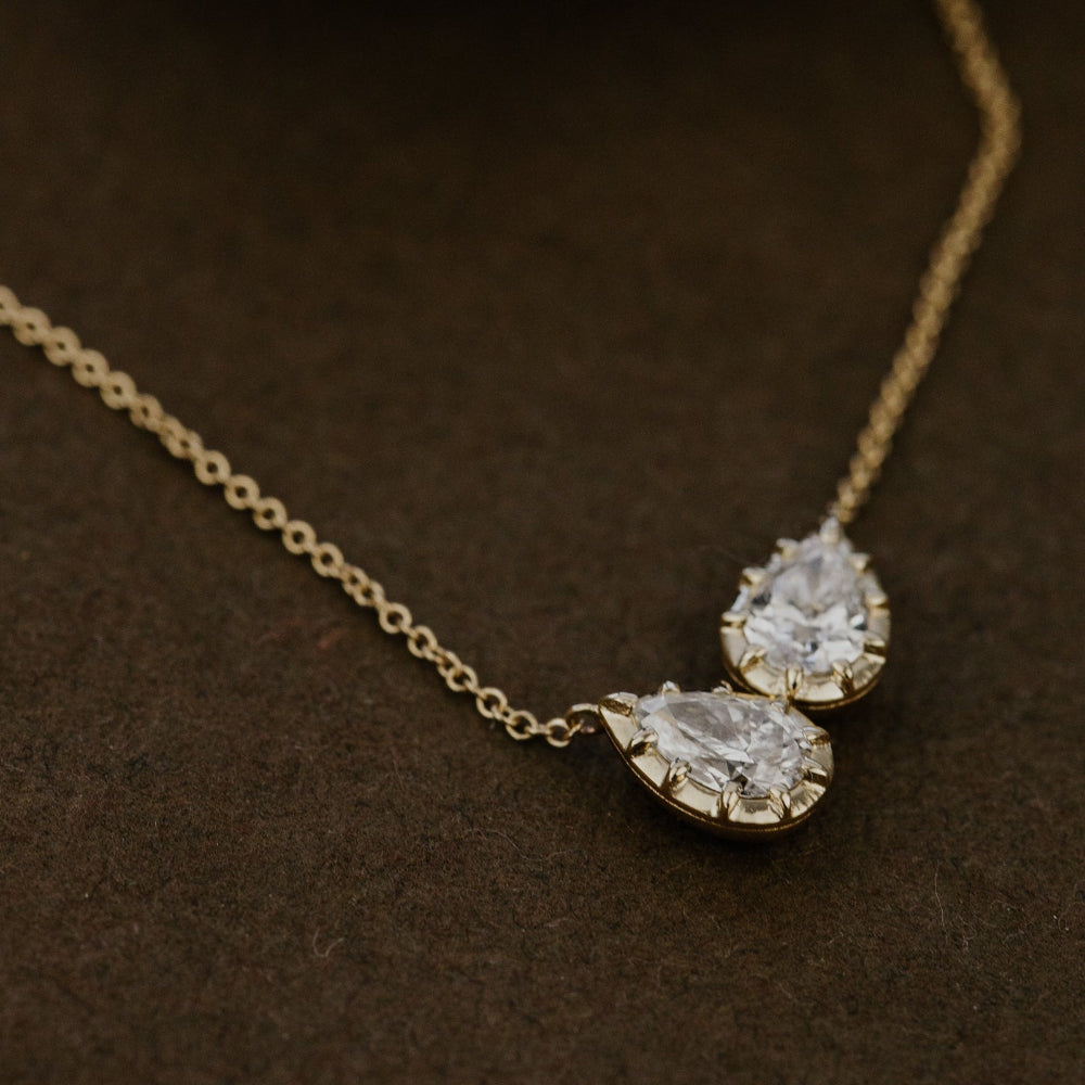 Gold necklace with two pear-shaped lab grown diamond pendants on a brown surface.