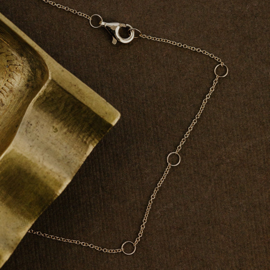 Yellow gold chain necklace on a brown surface with a textured green object.