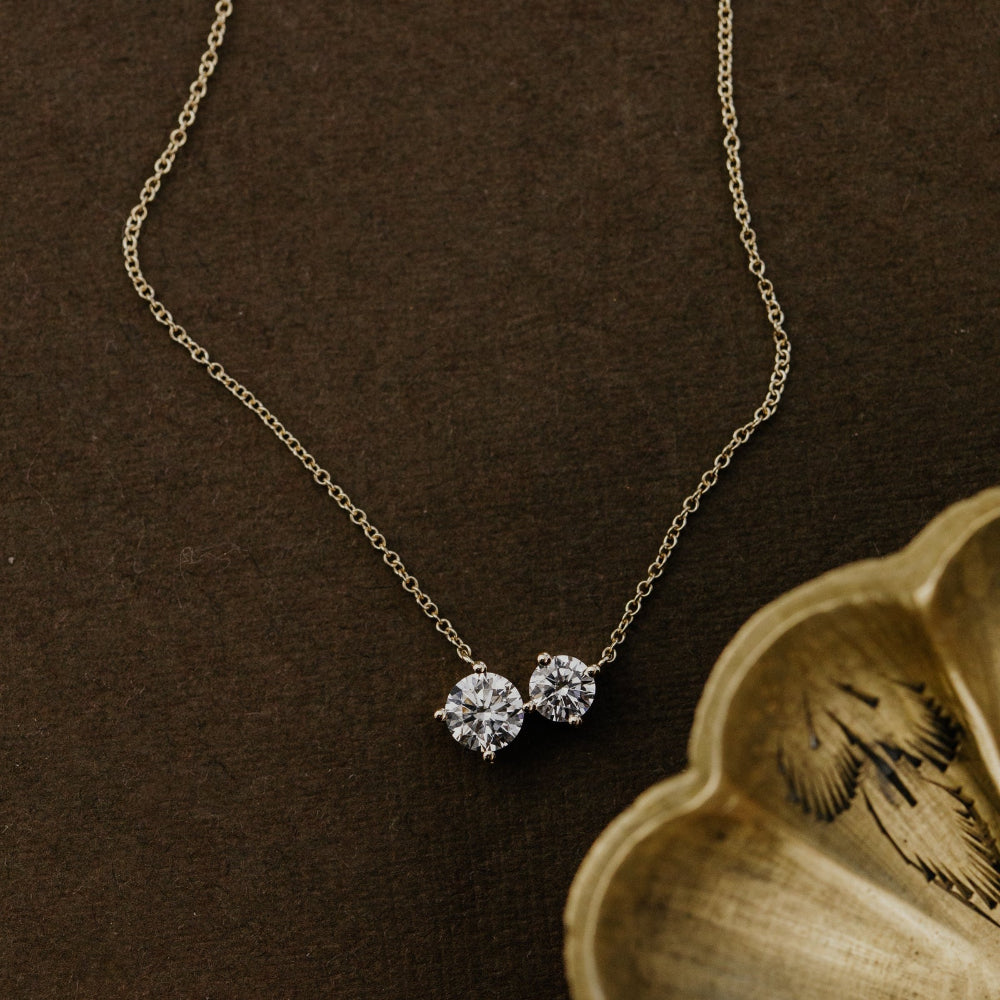 Gold necklace with a two round lab grown diamonds on a brown background.