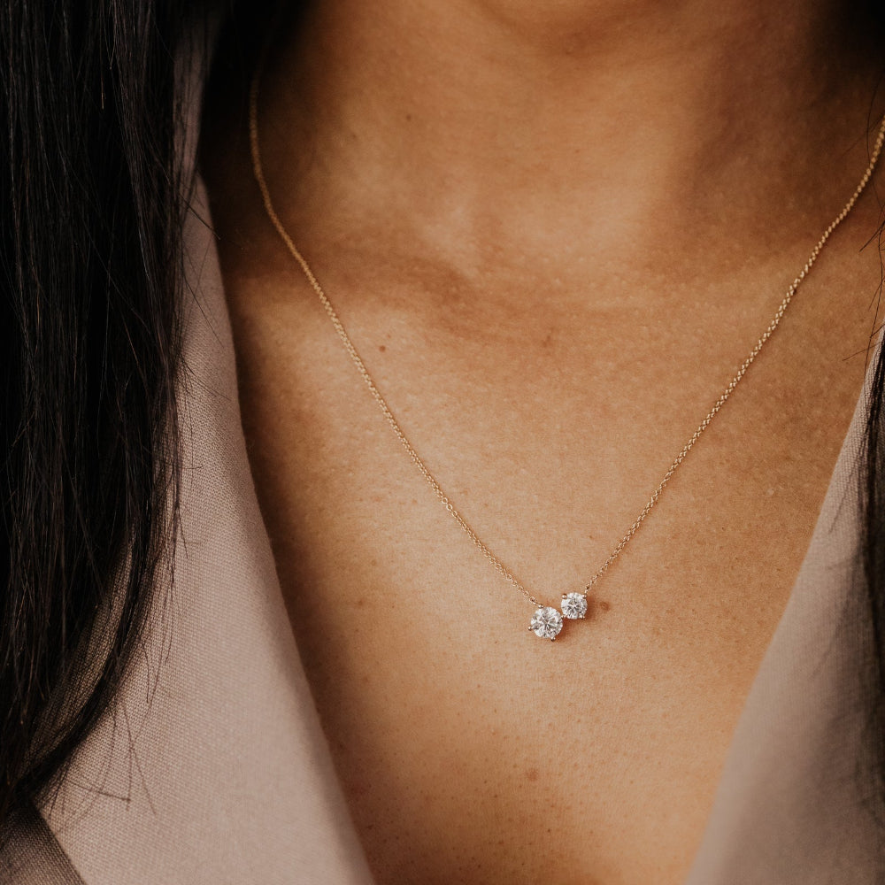 Close-up of a gold necklace with two round lab grown diamond pendants on a person's neck.