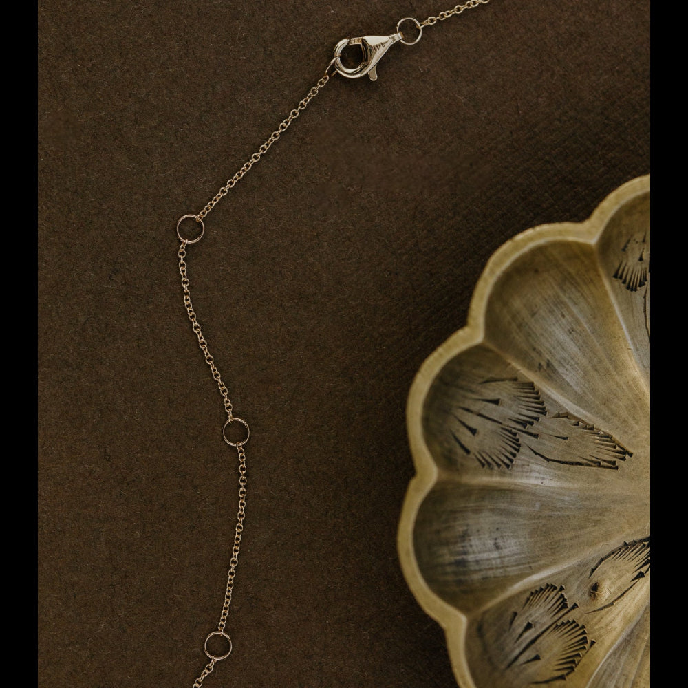 Gold chain necklace on a textured brown surface with a wooden leaf-shaped object.