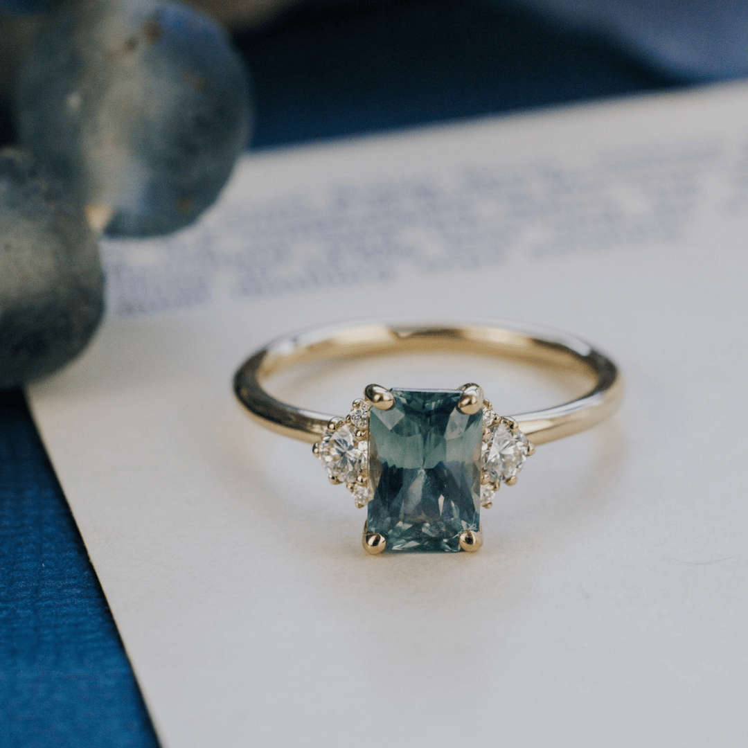 A 14k gold ring featuring a blue sapphire gemstone, displayed on a white surface with a soft-focus background.
