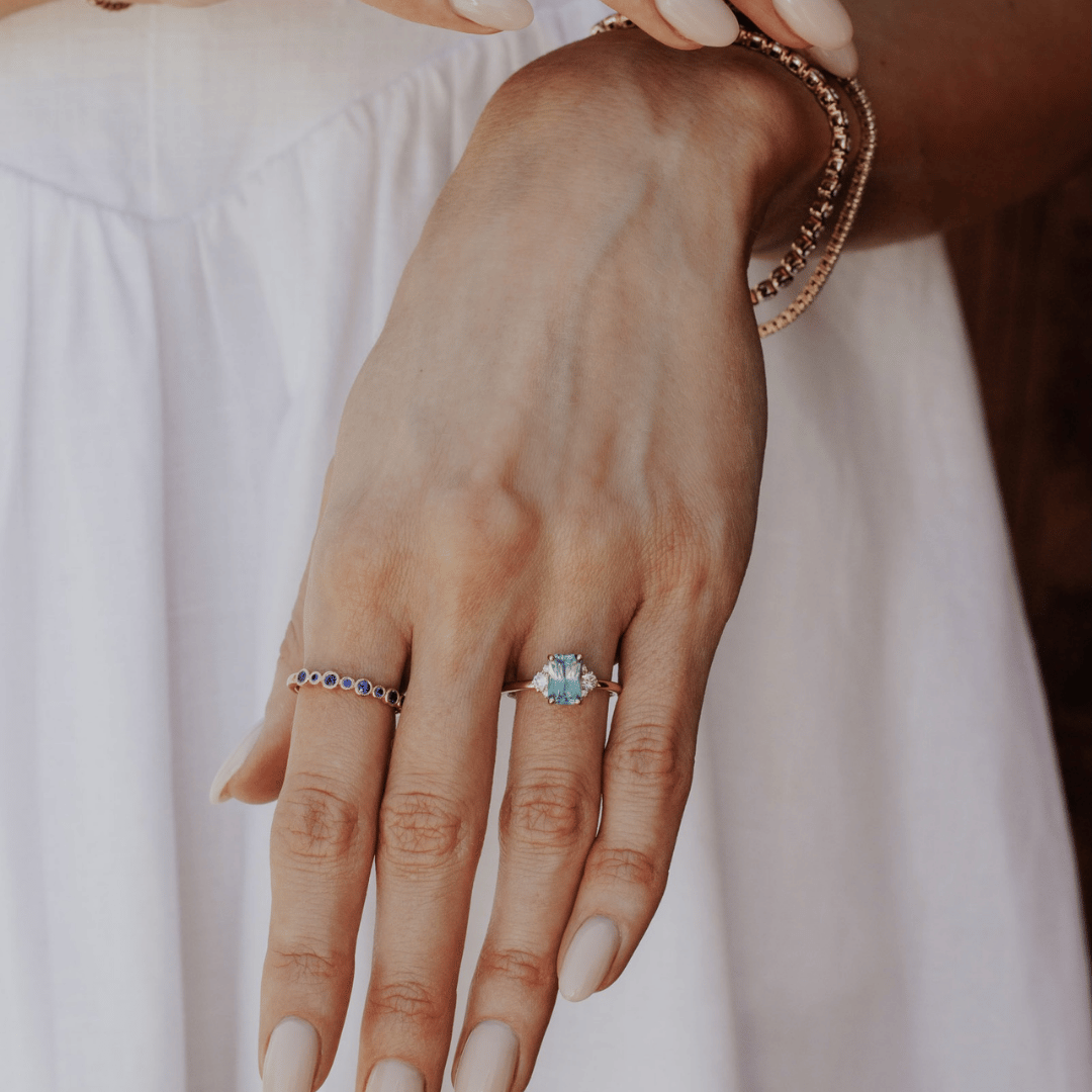 A 14k gold ring featuring a blue sapphire gemstone, displayed on the ring finger of a hand model.