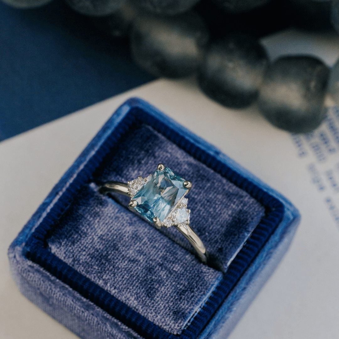 A 14k gold ring featuring a blue sapphire gemstone in a ring box, displayed on a white surface with a soft-focus background.