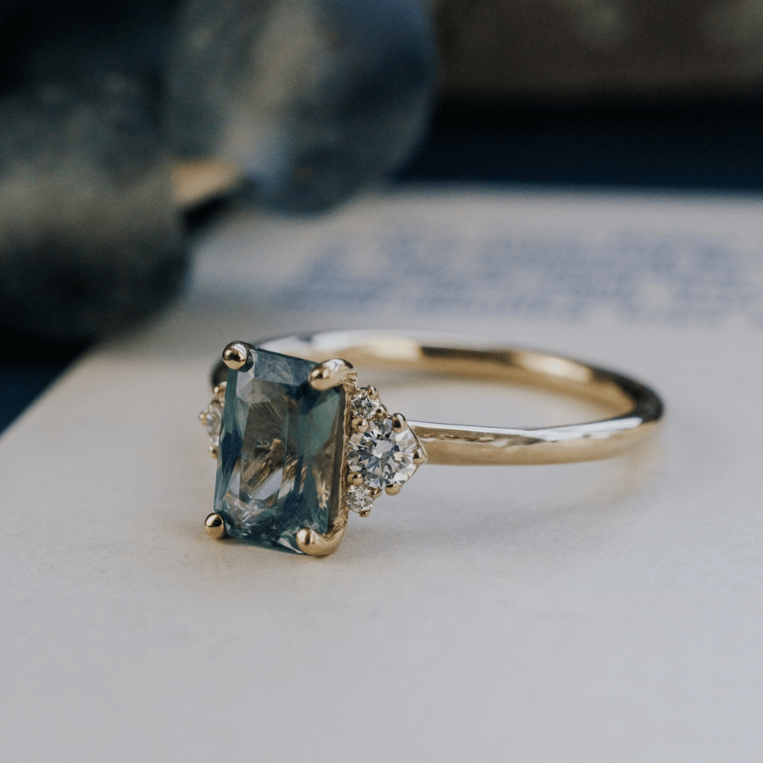 A 14k gold ring featuring a blue sapphire gemstone, displayed on a white surface with a soft-focus background.