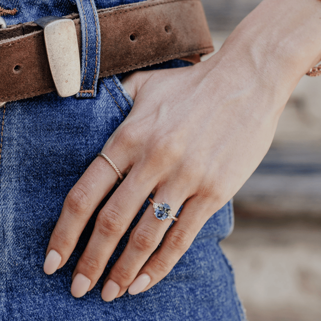 A 14k gold ring featuring a blue sapphire gemstone viewed from straight on, displayed on the ring finger of a hand model.